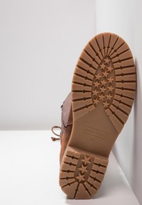 Brązowy zamszowy but z teksturowaną gumową podeszwą z wzorem gwiazd. Nazwa marki „ANNA FIELD” oraz rozmiar „37” są wytłoczone na podeszwie.