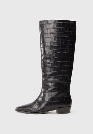 Botas de couro pretas até ao joelho com textura de crocodilo, bico fino e salto baixo em bloco. Apresentam uma discreta marcação perto do tornozelo.