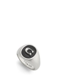 Silverring med en svart oval mittdel och en framträdande metallikon. Slät, rundad design med ingraverad "COACH"-detalj.