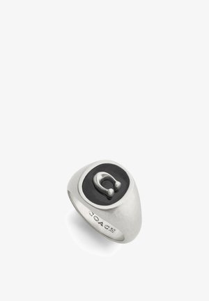 Bague en argent avec un centre ovale noir et un emblème métallique proéminent. Design lisse et arrondi avec un détail gravé "COACH".