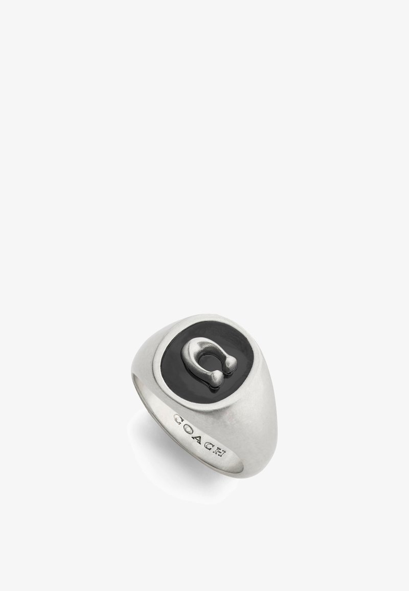 Silverring med en svart oval mittdel och en framträdande metallikon. Slät, rundad design med ingraverad "COACH"-detalj.