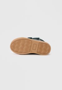 Dunkelgrüner Schuh mit strukturiertem Obermaterial, Klettverschluss, Gummisohle und einem gemusterten Profil. Verfügt über eine flache Ferse für Stabilität.