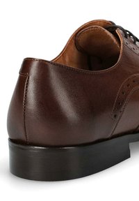 Brązowe skórzane buty formalne o gładkiej powierzchni, zaokrąglonym obcasie i dekoracyjnych perforacjach po bokach. Czarna podeszwa kontrastuje z górą.