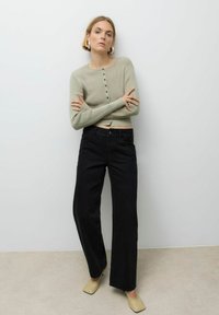 Kerge rohelise värvi ribakoe särk, millel on nööpidega kinnitused; koos kõrge vöökohaga sirgete mustade teksade ja beežide terava ninaga kontsakingadega.