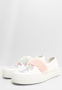 Białe wsuwane trampki z kolorowymi ilustracjami jednorożców. Posiadają puszyste, pastelowo różowe i zielone akcenty na przedniej części buta. Gruba podeszwa.