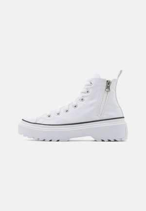 Zapatilla alta de lona blanca con superficie texturizada, puntera de goma, cremallera lateral y suela blanca gruesa con líneas de acento negras.