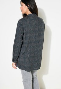 Dunkelblaue Bluse mit einem strukturierten Muster aus kleinen, bunten Punkten. Sie hat einen Kragen, lange Ärmel und eine lockere Passform.