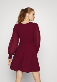 Burgundi kleit pikka läbipaistvate puhvvarrukatega, istuv kehaosa, laienev seelik ja selja lukuga detail. Sile tekstuur ja voolav disain.