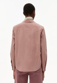Camicia button-up a righe in rosa polveroso con una sottile lucentezza, dotata di un yoke posteriore, maniche lunghe e orlo arrotondato, abbinata a pantaloni chiari.