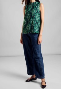 Ärmlös grön topp med ett geometriskt mönster, matchad med mörkblå vida jeans och svarta ballerinaskor, med rundad halsringning.