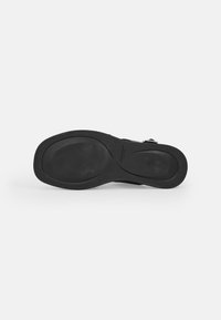 Black rubber shoe sole with a smooth texture, featuring a rounded shape and slight curvature. Includes embossed branding detail.