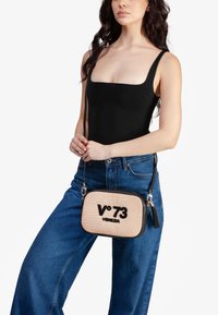 Geweven beige schoudertas met zwarte accenten, met het logo "V°73 VENEZIA" in bold, en een afneembare zwarte kwast aan de rits.