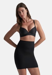 Reggiseno nero e gonna alta coordinata, entrambi realizzati in un tessuto liscio e lucido. Il reggiseno presenta spalline sottili e un design senza cuciture.