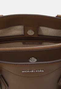 Wnętrze brązowej torebki skórzanej z beżowym wykończeniem tekstylnym, kieszonka na zamek błyskawiczny oraz zapięcie na zatrzask. Posiada logo 'MICHAEL KORS'.