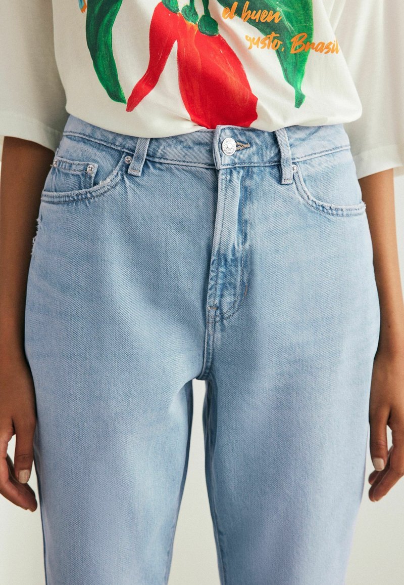 Jeans din denim de un albastru deschis, cu talie înaltă, dotate cu buzunare frontale și închidere cu buton. Textură netedă, cu detalii minime de uzură.