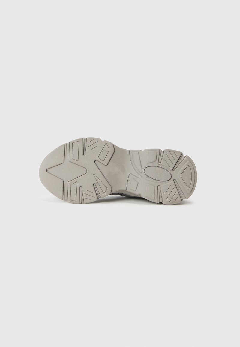 Suola di sneakers grigia chiara con un motivo testurizzato, caratterizzata da dettagli a incavo, una punta arrotondata e una costruzione robusta in gomma.