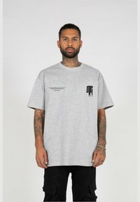 Grå oversized T-shirt lavet af bomuld, med korte ærmer, rund halsudskæring og sorte grafiske detaljer på forsiden.