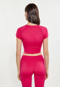 Crop top aderente a maniche corte e leggings a vita alta di colore rosa brillante, realizzati in un tessuto liscio e elasticizzato, con un design minimalista.