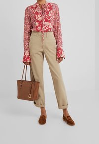 Blommig röd blus med knutkrage, beige byxor, brun läderhandväska med guldaccenter och bruna mockaskor.