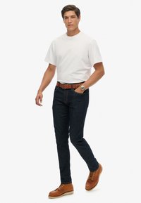 Biała bawełniana koszulka, niebieskie dżinsy z denimu, brązowy skórzany pasek i brązowe sznurowane buty. Casualowy strój o prostym kroju i dopasowanym fasonie.