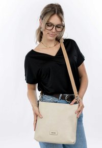 Beige textured crossbody bag with a rectangular shape, featuring a detachable leather strap and a metallic logo accent on the front.