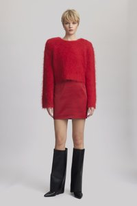Piros, bolyhos pulóver, amely doboz alakú, piros, testhezálló mini szoknyával párosítva. A modellen magas, fekete, magassarkú csizmák vannak, sima bőrből készült kivitelben.