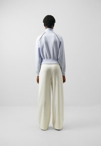 Jersey azul claro con cuello alto, dobladillo elástico, combinado con pantalones anchos color crema. Textura suave con acentos en contraste a lo largo de los hombros.