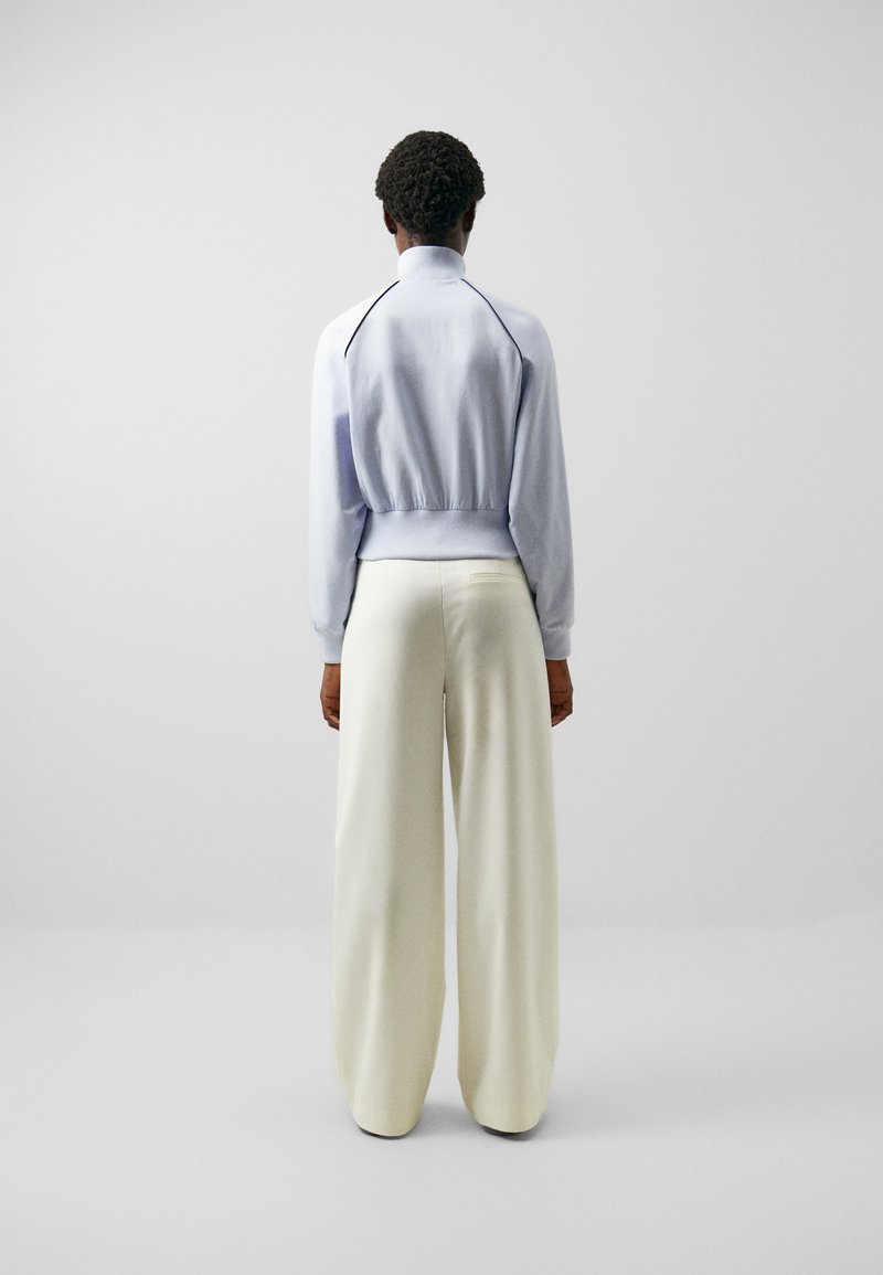 Helles blaues Pullover mit hohem Kragen, elastischem Saum, kombiniert mit weit geschnittenen cremefarbenen Hosen. Glatte Textur mit kontrastierenden Akzenten entlang der Schultern.