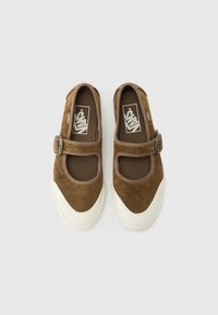 Pantofi maro din piele întoarsă, stil Mary Jane, cu talpă albă din cauciuc, prevăzuți cu o curea și o cataramă peste laba piciorului, și cu căptușeală textilă.