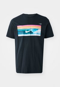 Svart bomulls T-skjorte med et grafisk motiv av en bølge med blå og rosa detaljer og en hvit Nike-logo i midten. Korte ermer, rund hals.