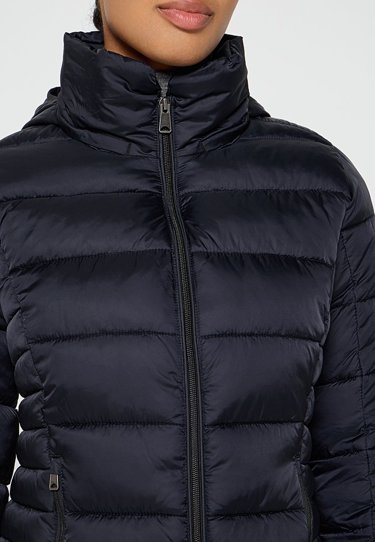Giacca imbottita blu navy con colletto alto, caratterizzata da sezioni trapuntate orizzontali, una cerniera frontale completa e due tasche laterali con cerniera.