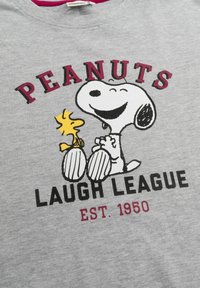 T-shirt grigio in cotone con una grafica di Snoopy e Woodstock. La scritta recita "PEANUTS LAUGH LEAGUE EST. 1950," in nero e bordeaux.