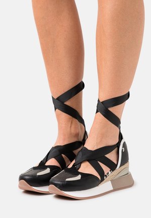 Black sneakers with crisscross black ribbon straps, textured leather, a wedge sole, and a white and beige accent detail.
