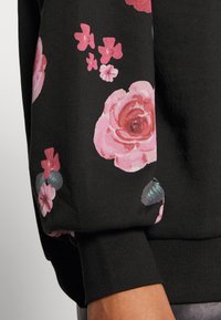 Černá mikina s barevnými květinovými vzory v růžové a fialové barvě, s žebrovanými manžetami a měkkou, texturovanou látkou.