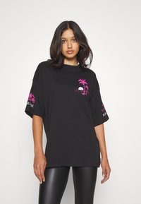 Oversized sort t-shirt i bomuld med grafisk tryk af en pink palme og solnedgang foran samt stiliseret tekst på ærmet. Korte ærmer.