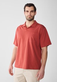 Röd polo t-shirt av mjukt tyg, med klassisk krage, kortärmade och bröstficka på vänster sida. Avslappnad passform och slät textur.