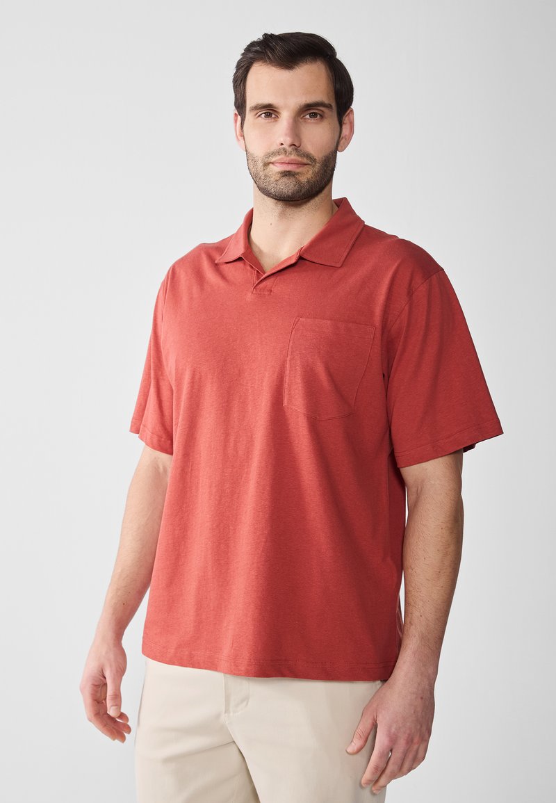 Röd polo t-shirt av mjukt tyg, med klassisk krage, kortärmade och bröstficka på vänster sida. Avslappnad passform och slät textur.
