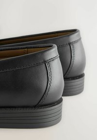 Zwarte leren instappers met een gladde textuur, ronde randen, contrasterende stiksels en een geprofileerde rubberen zool voor grip.