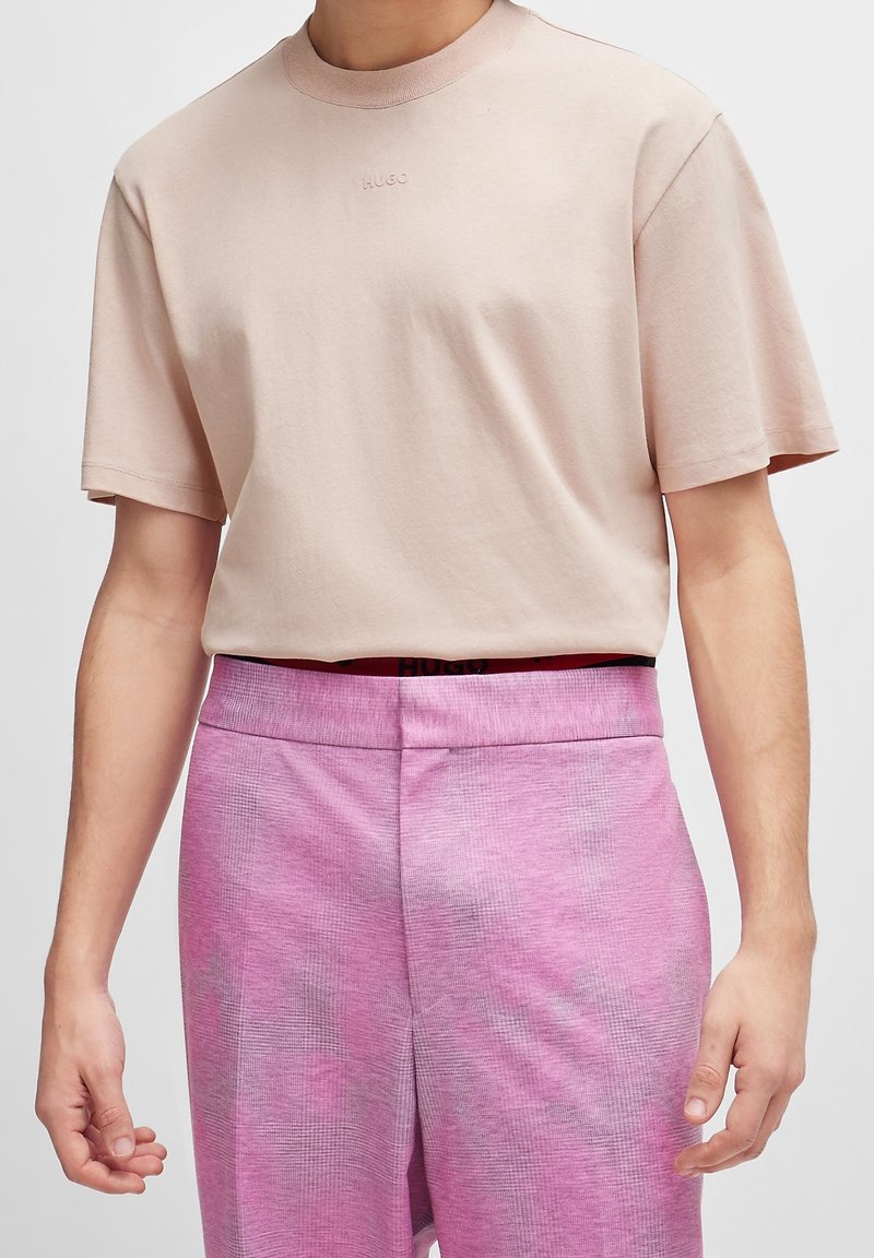 T-shirt en coton rose clair avec col rond et manches courtes. Logo "HUGO" brodé sur la poitrine. Assorti à un short rose texturé.