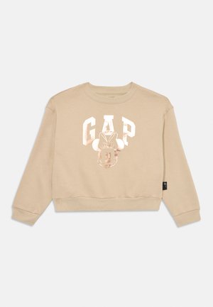 Beige cropped sweatshirt, featuring metallic silver "GAP" text and Minnie Mouse design on the front. Ribbed cuffs and hem. Soft fabric texture.