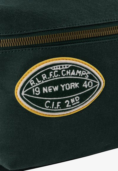 Zeleno platneno vrečko z rumeno in belo ovalno nalepko. Besedilo na nalepki vključuje "R.L.R.F.C. ŠAMPIONI," "19 NEW YORK 40," in "C.I.F 2. " Zlati zadrga.