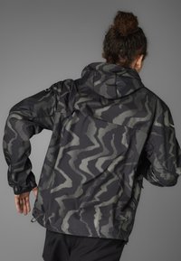 Wasserabweisende schwarze Jacke mit einem wellenförmigen Punktmuster in Grau. Verfügt über eine Kapuze, lange Ärmel und einen verstellbaren Saum für die optimale Passform.