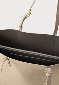 Geantă tote din piele bej cu suprafață texturată, având un interior gri și un buzunar cu fermoar auriu, completată de curele subțiri.