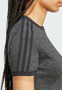 Černé sportovní tričko s krátkými rukávy a texturovaným povrchem, se třemi černými pruhy podél ramen. Materiál má jemný třpytivý efekt.
