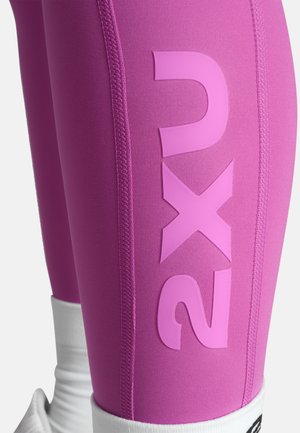 Roza športna legging hlače z gladko teksturo, ki na stegnu vsebujejo velik bel logotip "2XU", kontrastno šivanje in bel manžetni rob ob gležnju.