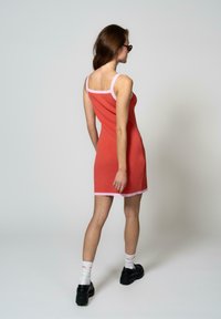 Abito lavorato a maglia in corallo con rifiniture rosa, presenta spalline sottili e una silhouette aderente, che termina sopra il ginocchio con una texture a coste.