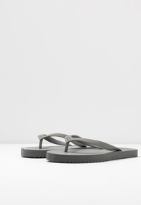 Hallid hallid sussid, mis on valmistatud kummist, omavad tekstuuritud rihma, lamedat tallat, millel on zick-zack detailid, ja minimalistlikku disaini.