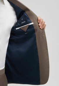 Brauner Anzugjacke mit einem navyblauen Satin-Innenfutter. Verfügt über ein Einstecktuch und markierte Etiketten. Taillierte Passform mit leichten Stickdetails.
