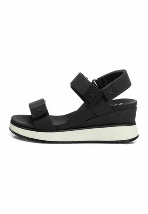 Las sandalias de cuña negras cuentan con dos correas ajustables, una parte superior sintética suave y una entresuela blanca en contraste con una suela texturizada.