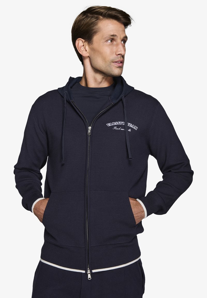 Marineblå zip-up sweatshirt i strikstof med to forlommer, justerbar snor i hætten og kontrasterende hvide ribbede manchetter og kant.